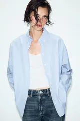 Camisa de manga larga con patrón de rayas verticales en tonos celeste y blanco, cuello con solapa abotonada y un bolsillo aplicado en el pecho. Cierre frontal con botones blancos.
