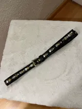 Cinto de cuero negro con hebilla metálica y tachas decorativas en tonos plateados y dorados a lo largo de toda la tira.