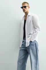 Camisa de corte slim fit confeccionada en tejido de algodón con textura. Presenta cuello italiano, manga larga con puños abotonados y cierre frontal de botones.