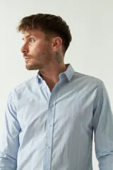 Camisa de hombre de corte slim fit, confeccionada en algodón con diseño de rayas verticales finas en tonos claros. Presenta cuello clásico, cierre frontal con botones y logo bordado en el pecho.
