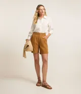 Bermuda color ocre de sarga, con cintura alta elástica, cierre con botón y cremallera, bolsillos laterales y pliegues delanteros.