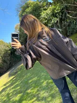 Camisa oversize a rayas marrón y negro, con cuello camisero, bolsillo frontal grande con bordado rojo de un caballo, y mangas abullonadas con puños elásticos.