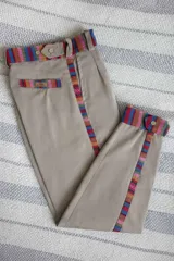 Bombacha de campo marrón de tiro medio, con detalles de tejido guarda pampa multicolor en la cintura, laterales y bolsillos traseros. Cuenta con cierre reforzado y botón de madera.