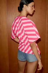Top de algodón con estampado de rayas diagonales en tonos fucsia y rosado. Presenta cuello redondo, mangas cortas tipo murciélago y un diseño de bajo asimétrico.