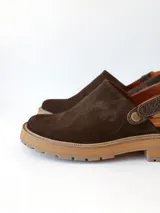 Zueco de cuero gamuzado color chocolate, con diseño de punta cerrada y tira ajustable con hebilla metálica en el talón. Presenta una suela de plataforma dentada en tono marrón claro.