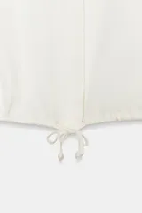 Camisa de satén con cuello solapa, manga larga con puños y bajo ajustable mediante cordones. Presenta cierre frontal con botones ocultos.