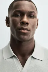 Jersey de punto color verde oliva, de calce relajado (relaxed fit), con cuello solapa y abertura frontal en forma de V. Es de manga corta y presenta acabados en rib en puños y ruedo.