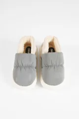 Pantufla tipo slip-on con diseño acolchado, combinando paneles en color gris y beige. Cuenta con interior forrado en material suave y suela de goma blanca.