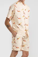 Short de algodón color crema con estampado de sirenas color naranja y amarillo, cintura elastizada con cordón ajustable, dos bolsillos laterales y un bolsillo trasero tipo parche.