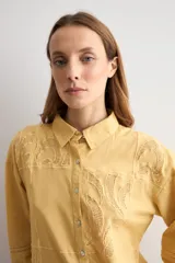 Camisa amarilla de manga larga con detalles bordados y calados en los hombros, pecho y mangas, corte clásico con cuello camisero y cierre frontal de botones.
