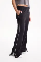 Pantalón deportivo negro de corte wide leg, sin frisa, con ribete blanco en los laterales y aberturas con botones en los tobillos.