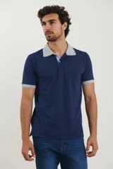 Remera polo azul marino con cuello y puños de manga corta en gris claro. Presenta una tapeta de dos botones con un detalle de rayas azules y blancas en el interior, y un bolsillo en el pecho con un logo bordado.