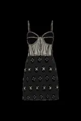 Vestido corto negro sin mangas confeccionado en terciopelo y tul transparente, con corsé estructurado con ballenas y tirantes finos. Presenta detalles de pedrería y bordados brillantes en las copas, los tirantes, las costuras frontales y a lo largo de la falda de encaje.