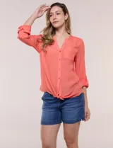 Blusa de calce relajado color salmón, confeccionada en tela liviana con textura sutil. Presenta escote en V con abotonadura frontal, bolsillo parche en el pecho, mangas largas regulables con presilla y ruedo con opción de anudar en el frente.