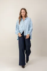 Camisa de corte oversize y diseño holgado, color celeste con estampado de pequeños corazones negros. Presenta cuello clásico, cierre frontal con botones y mangas largas abullonadas con puños ajustados.