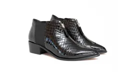 Botin de cuero negro con acabado charol y textura de reptil. Presenta cierre frontal con cremallera, paneles laterales elásticos y tacón bajo de bloque.