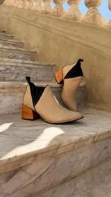 Botinetas de cuero color beige claro con inserciones elásticas laterales en negro y taco cuadrado de madera. Presentan punta fina y tirador trasero.
