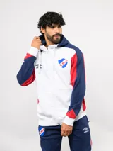 Campera deportiva Umbro del Club Nacional de Football, con cierre frontal, capucha ajustable con cordones y diseño en bloques de color azul, celeste y blanco. Presenta el logo de la marca y el escudo del club bordados en el pecho.
