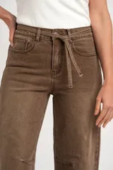 Pantalón jean de corte barrel y tiro alto, en tono marrón lavado, con bolsillos laterales y traseros, y lazo ajustable en la cintura.