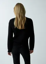 Jersey negro de punto de corte holgado, con cuello en V adornado con detalles de encaje y manga larga.