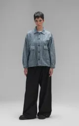 Campera de denim rígido con textura de trama única, corte oversize, cuello camisero, cierre frontal con botones y bolsillos delanteros con solapa.
