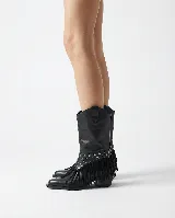 Bota de cuero negro estilo texano, con taco bajo y punta fina. Incluye un aplique desmontable en la zona del empeine decorado con tachas metálicas y flecos largos.