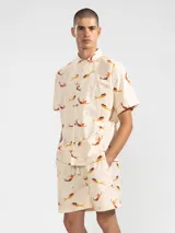 Bermudas de algodón color crema con estampado de sirenas en tonos naranja y marrón. Tiene cintura elástica con cordón ajustable, dos bolsillos laterales y un bolsillo trasero.