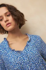 Blusa blanca con finas rayas verticales negras, de manga corta con volados y escote en V con pequeños botones y detalle de volado en el borde.