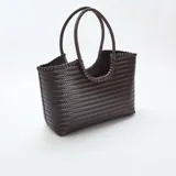 Bolso de mano grande con diseño rectangular y textura trenzada en color marrón oscuro. Cuenta con dos asas circulares trenzadas integradas en la estructura.