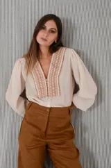 Camisa de voile de algodón color arena, con cuello en V decorado con aplique de guarda con punto smock, mangas largas abullonadas con puños elásticos y cierre frontal con pequeños botones de nácar.
