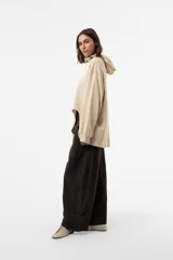 Buzo de punto oversize en color beige, con capucha, cordones largos ajustables y mangas largas amplias con puños elásticos. Presenta diseño asimétrico, más largo en la parte posterior.