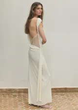 Vestido largo recto color crudo, con cuello redondo, manga corta, detalle drapeado en la cintura y espalda abierta.