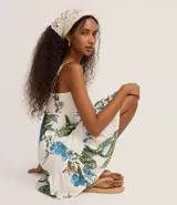 Vestido corto de corte evasé confeccionado en tejido laise con estampa tropical de flores azules y hojas verdes. Presenta escote en V, breteles finos ajustables y diseño con perforaciones caladas características del broderie.