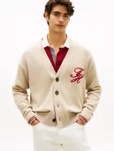 Cárdigan de punto grueso en color beige, con cuello en V, cierre frontal con botones y bolsillos de ojal. Presenta puños y bajo acanalados con líneas rojas y blancas, y un logo script bordado en rojo en el pecho.
