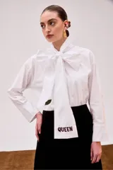 Camisa blanca de algodón pima con cuello mao y lazos para anudar. Presenta un bordado de labios y la palabra 'Queen' en color borgoña.