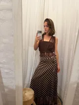 Pollera midi tipo pareo de satén color chocolate con estampado de lunares blancos. Presenta un diseño envolvente con ajuste lateral y un ruedo con detalle de microtul y puntilla bordada.