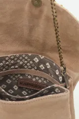 Cartera de mano o bandolera pequeña de gamuza negra con solapa decorada con un bordado artesanal en tonos dorados y beige que simula un pájaro con alas extendidas. Posee cadena metálica color dorado viejo y cierre magnético.