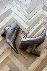 Botín de cuero vacuno color bronce metalizado, con diseño acordonado, cierre lateral interno y taco cuadrado.