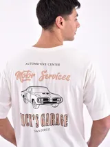 Remera color crudo de corte oversize con estampa en la espalda de un auto clásico, texto 'Automotive Center Motor Services' y 'Nick's Garage San Diego'.