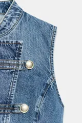 Top de denim blanco sin mangas, con cuello mao y cierre frontal cruzado con trabillas y botones metálicos.