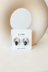 Aros tipo argolla de acero quirúrgico plateado con un dije de piedra natural esférica en color oscuro. Diseño minimalista y versátil.