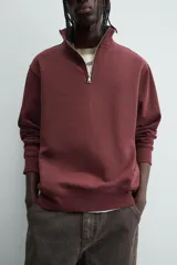 Sudadera roja de corte regular, con cuello alto y cierre frontal de cremallera. Manga larga y terminaciones en rib.