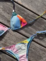Bikini color dorado brillante, con corpiño triangular de atar al cuello y espalda, con almohadillas desmontables. La bombacha es vedetina con tiras ajustables a los costados.
