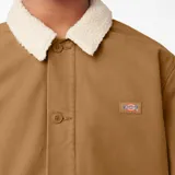 Campera Dickies color marrón con cuello de corderito blanco, cierre con botones a presión, bolsillos laterales y logo de la marca en el pecho.