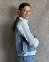 Chaleco de corte recto y largo a la cintura, confeccionado en denim con estampado de rayas verticales en tonos azul y blanco. Presenta cuello redondo y costuras visibles que definen su estructura.