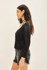 Cardigan negro con escote en V, manga larga y cierre frontal con botones. Presenta un diseño con aplicación de tachas plateadas distribuidas por toda la prenda.