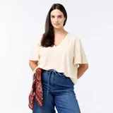 Camiseta de manga corta y cuello en V, confeccionada en tejido de punto calado con sutiles perforaciones geométricas, de corte holgado y diseño versátil.