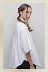 Camisa blanca de popelina 100% algodón, de diseño oversize y corte unisex. Presenta cuello clásico, manga amplia, bolsillo frontal y canesú con pliegue central en la espalda.