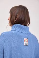 Sweater de punto color azul, con cuello alto y diseño de trenzas verticales. Presenta mangas largas con puños acanalados y un corte holgado.
