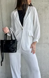 Blazer blanco con finas rayas verticales negras, solapas clásicas, cierre con un botón y bolsillos frontales.